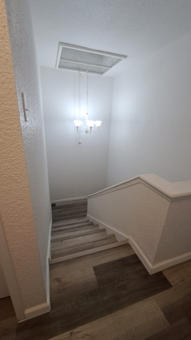 stairway with wood-type flooring and an inviting chandelier