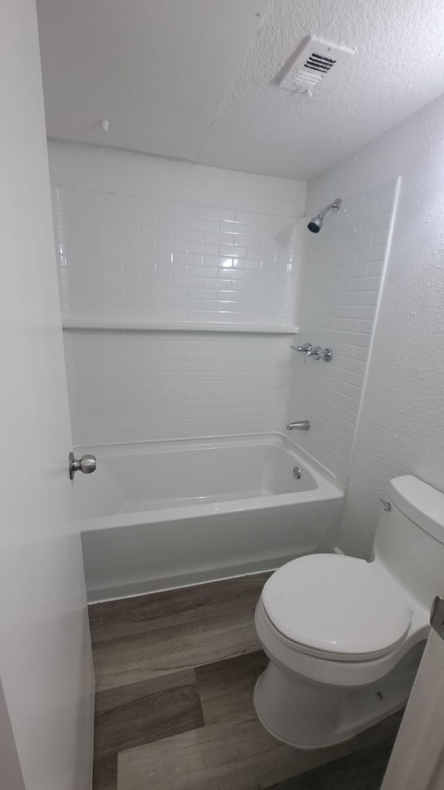 bathroom with a textured ceiling, hardwood / wood-style flooring, toilet, and tiled shower / bath