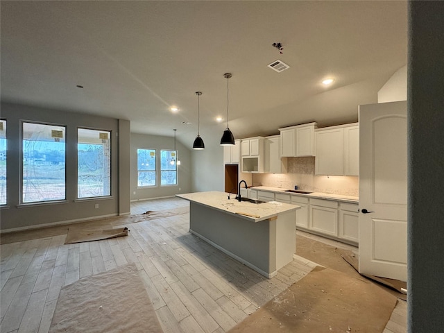 kitchen with black electric cooktop, sink, pendant lighting, white cabinetry, and an island with sink