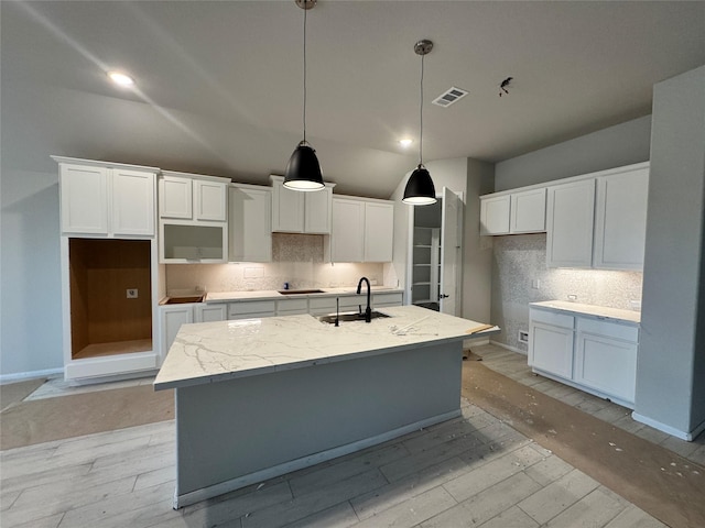 kitchen featuring light stone countertops, sink, decorative light fixtures, white cabinets, and an island with sink