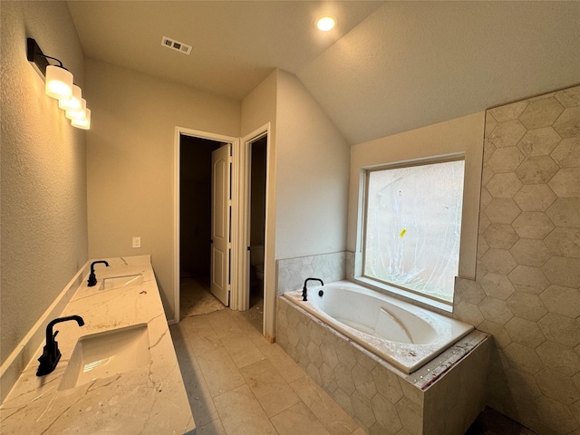 bathroom featuring vanity, lofted ceiling, toilet, tile walls, and tiled bath