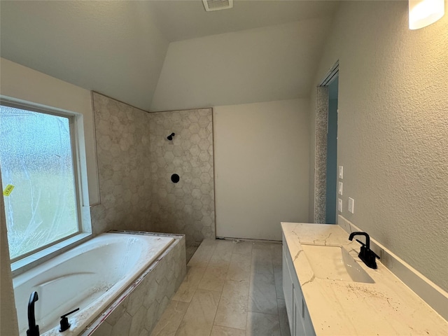 bathroom featuring vanity, tiled tub, and vaulted ceiling