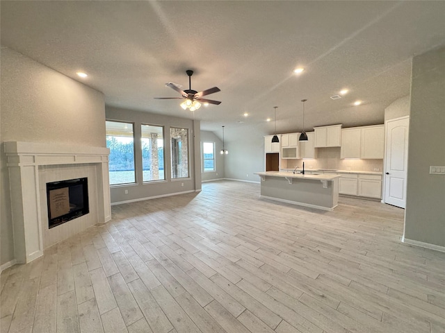 unfurnished living room with sink, light hardwood / wood-style flooring, a textured ceiling, ceiling fan, and a fireplace