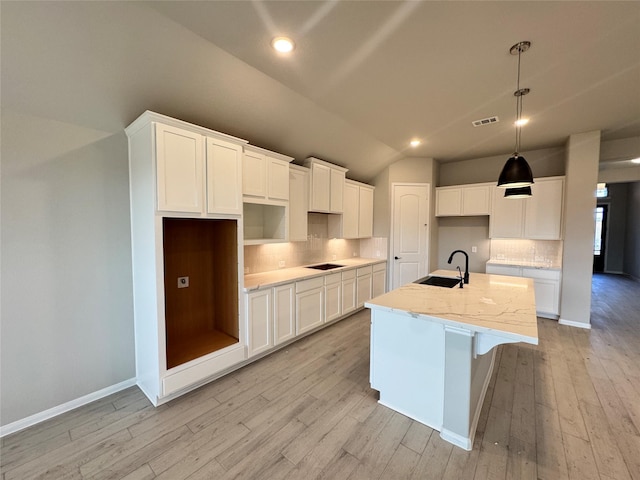 kitchen with white cabinetry, light stone countertops, sink, and a center island with sink