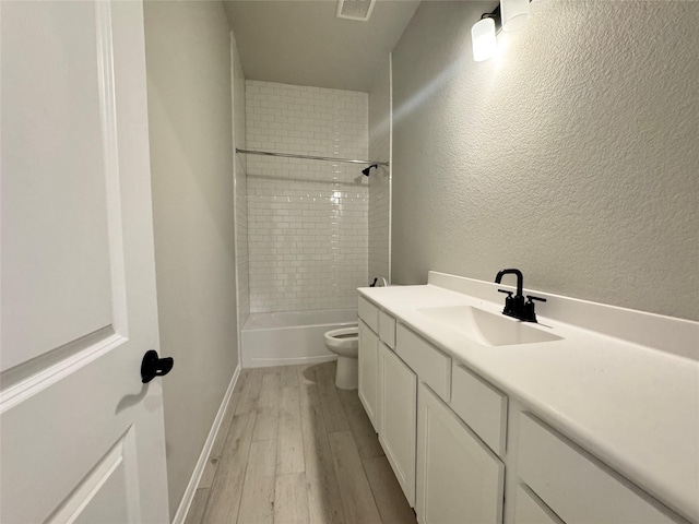 full bathroom with hardwood / wood-style flooring, tiled shower / bath, vanity, and toilet