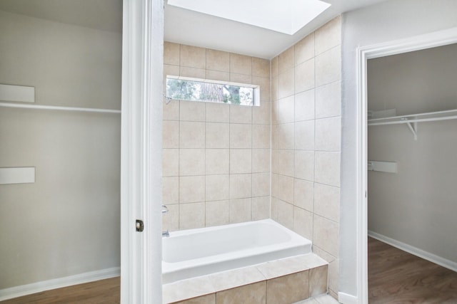 bathroom with tiled bath, hardwood / wood-style floors, and a skylight