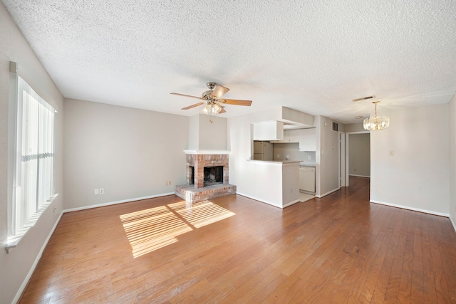 unfurnished living room with hardwood / wood-style floors, ceiling fan with notable chandelier, a textured ceiling, and a brick fireplace