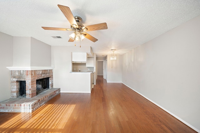 unfurnished living room featuring a fireplace, ceiling fan with notable chandelier, dark hardwood / wood-style floors, and a textured ceiling