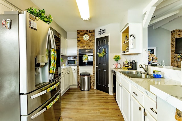 kitchen with appliances with stainless steel finishes, brick wall, sink, white cabinets, and light hardwood / wood-style floors