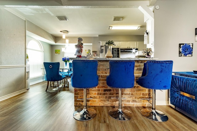 bar with white cabinets, hardwood / wood-style flooring, and stainless steel refrigerator