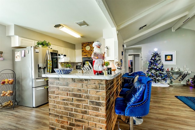 kitchen with lofted ceiling with beams, kitchen peninsula, stainless steel refrigerator with ice dispenser, light wood-type flooring, and white cabinetry