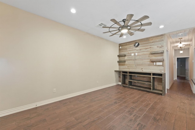 unfurnished living room featuring wooden walls, ceiling fan, and dark wood-type flooring