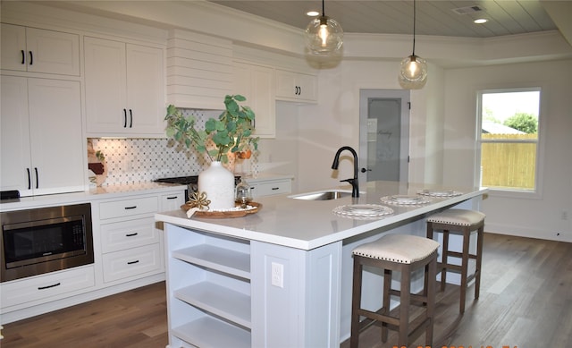 kitchen with stainless steel microwave, backsplash, a kitchen island with sink, sink, and hanging light fixtures