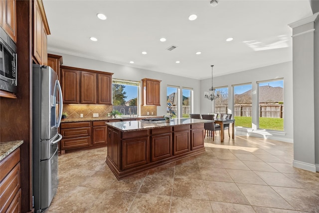 kitchen with pendant lighting, a center island, light stone countertops, appliances with stainless steel finishes, and tasteful backsplash