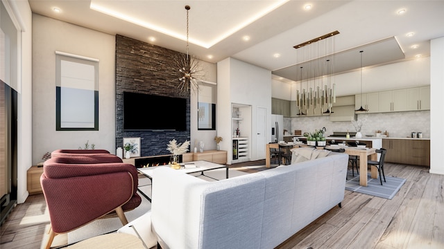 living room with an inviting chandelier, a raised ceiling, a high ceiling, and light hardwood / wood-style flooring