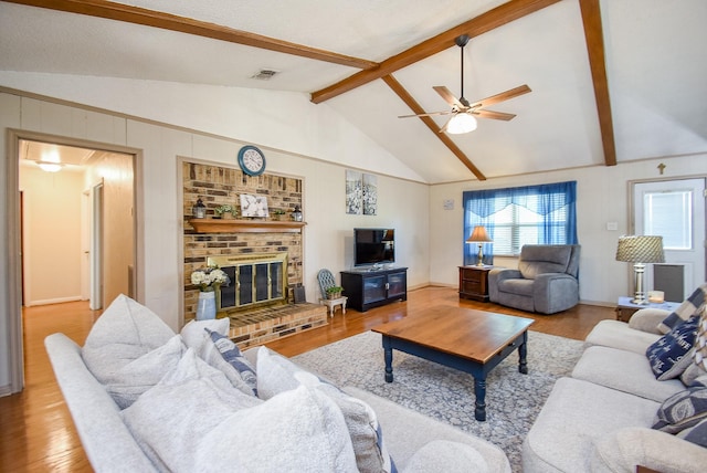 living room featuring light wood-type flooring, lofted ceiling with beams, a brick fireplace, and ceiling fan