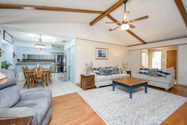 living room with vaulted ceiling with beams, ceiling fan with notable chandelier, and light hardwood / wood-style flooring