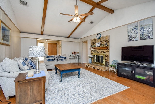 living room with vaulted ceiling with beams, hardwood / wood-style flooring, a brick fireplace, and ceiling fan