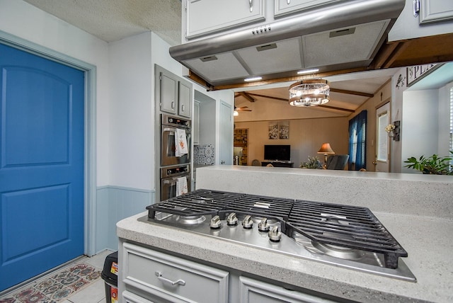 kitchen with vaulted ceiling with beams, stainless steel appliances, ceiling fan, and wood walls