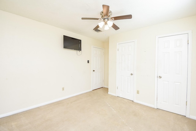 unfurnished bedroom featuring ceiling fan, light carpet, and two closets