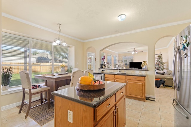 kitchen with ceiling fan with notable chandelier, sink, a center island, stainless steel refrigerator, and hanging light fixtures