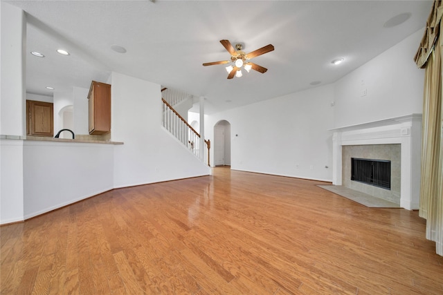 unfurnished living room with ceiling fan, sink, light hardwood / wood-style floors, lofted ceiling, and a tiled fireplace