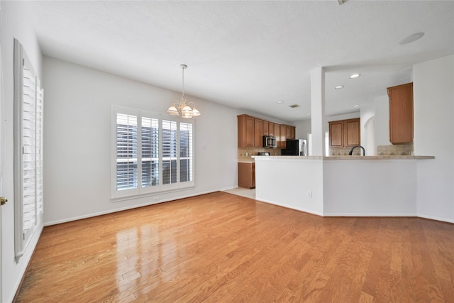 kitchen featuring decorative backsplash, an inviting chandelier, appliances with stainless steel finishes, and light hardwood / wood-style flooring