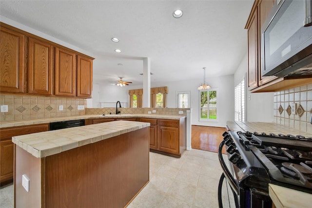 kitchen with tile countertops, kitchen peninsula, decorative backsplash, a kitchen island, and black appliances