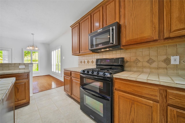 kitchen featuring gas stove, tasteful backsplash, light hardwood / wood-style flooring, a notable chandelier, and tile countertops