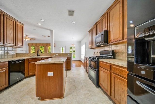 kitchen featuring tile countertops, black appliances, ceiling fan, tasteful backsplash, and a kitchen island