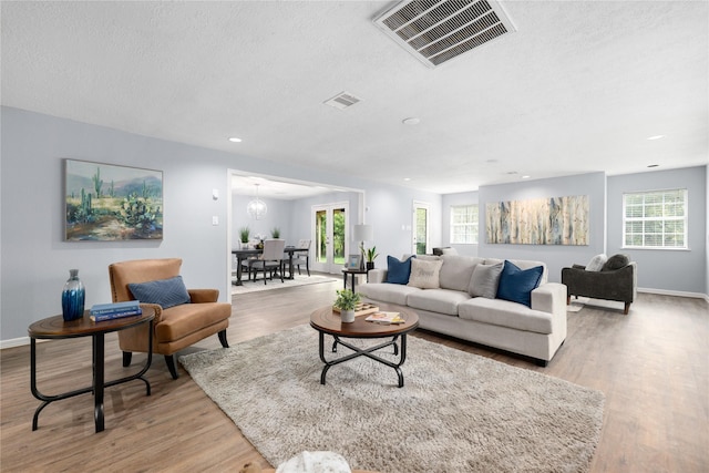 living room with a textured ceiling, an inviting chandelier, and light hardwood / wood-style flooring