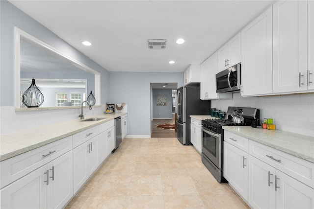 kitchen with white cabinetry, sink, stainless steel appliances, light stone counters, and decorative backsplash