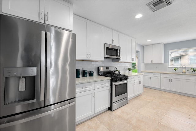 kitchen featuring white cabinets, appliances with stainless steel finishes, tasteful backsplash, and light stone counters