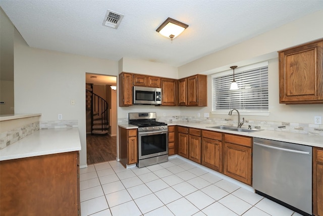 kitchen featuring sink, stainless steel appliances, hanging light fixtures, and a textured ceiling