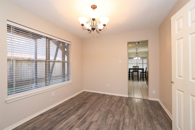 spare room featuring an inviting chandelier, dark wood-type flooring, and plenty of natural light