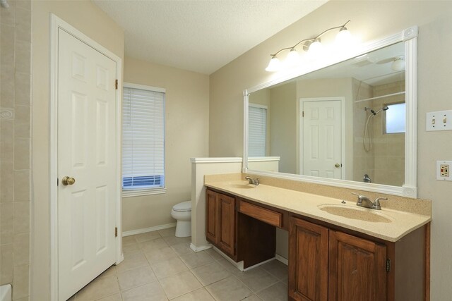 bathroom with tile patterned floors, toilet, a textured ceiling, a tile shower, and vanity