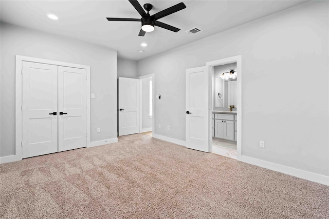 unfurnished bedroom featuring light carpet, a closet, ensuite bathroom, and ceiling fan