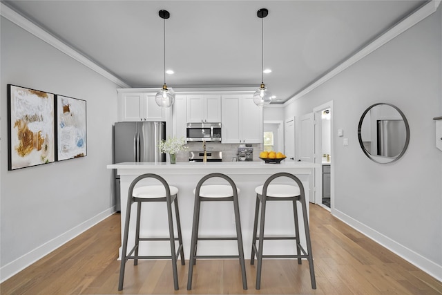 kitchen featuring a kitchen island with sink, white cabinets, decorative light fixtures, and appliances with stainless steel finishes