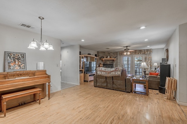 living room with a stone fireplace, light hardwood / wood-style flooring, and ceiling fan with notable chandelier