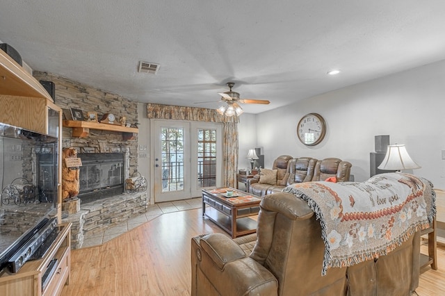 living room featuring a textured ceiling, light hardwood / wood-style floors, a stone fireplace, and ceiling fan