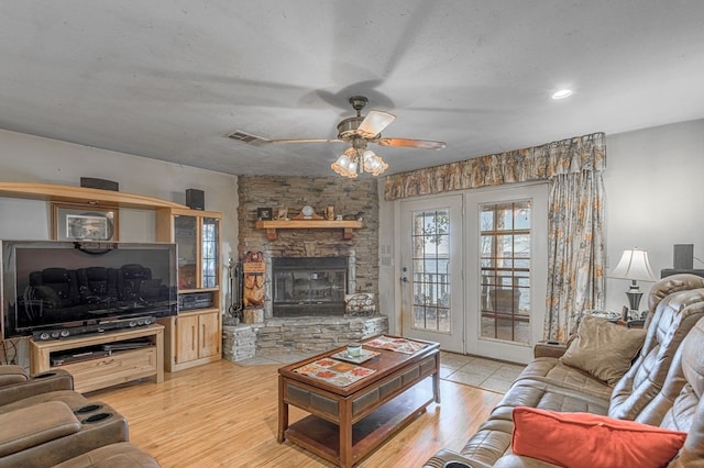 living room featuring ceiling fan, a stone fireplace, and light wood-type flooring