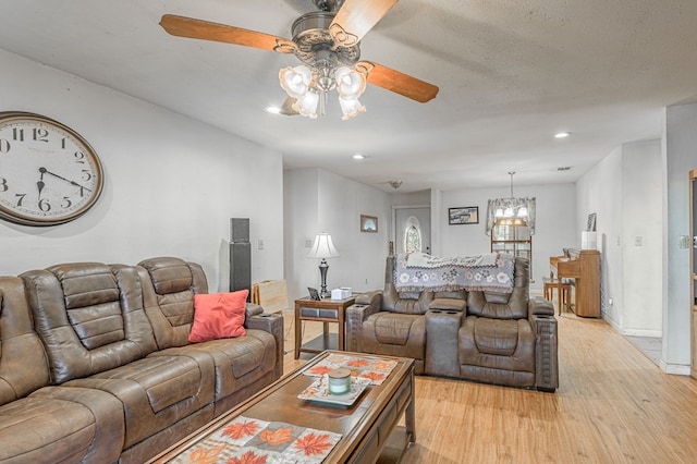 living room featuring ceiling fan with notable chandelier and light wood-type flooring