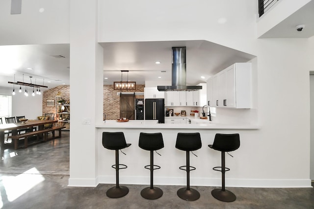 kitchen featuring brick wall, kitchen peninsula, island exhaust hood, black refrigerator, and white cabinets