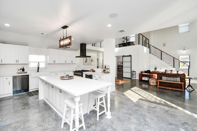 kitchen featuring stainless steel appliances, a barn door, ventilation hood, pendant lighting, and white cabinets