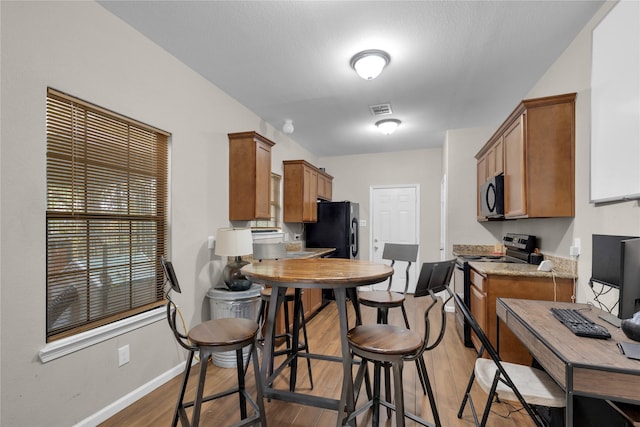 kitchen with light stone counters, black refrigerator, light hardwood / wood-style floors, and stainless steel range with electric stovetop