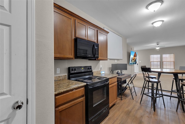 kitchen with ceiling fan, black appliances, stone countertops, and light hardwood / wood-style floors