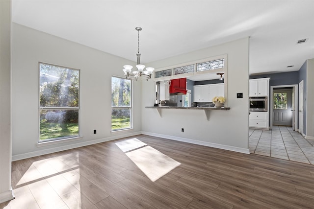 unfurnished dining area with hardwood / wood-style flooring, an inviting chandelier, and a wealth of natural light