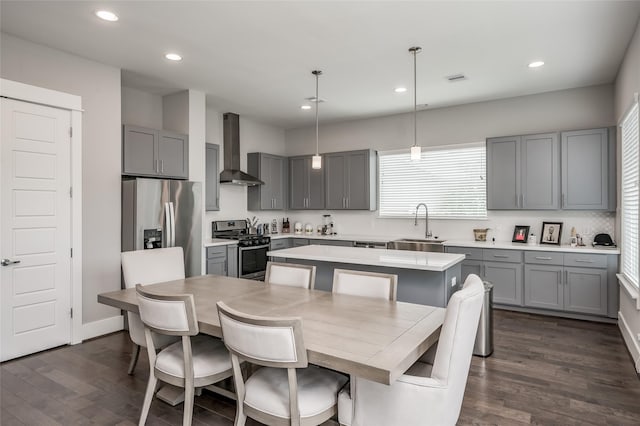 kitchen featuring wall chimney exhaust hood, appliances with stainless steel finishes, decorative light fixtures, a kitchen island, and dark hardwood / wood-style flooring