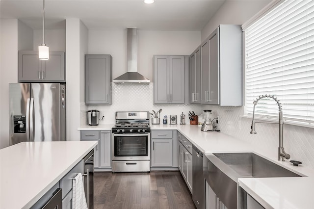 kitchen featuring appliances with stainless steel finishes, dark hardwood / wood-style flooring, sink, wall chimney range hood, and hanging light fixtures