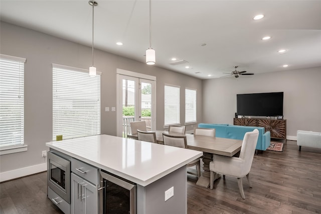 kitchen featuring stainless steel microwave, wine cooler, decorative light fixtures, a kitchen island, and dark hardwood / wood-style flooring